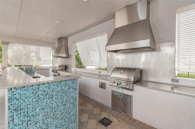 kitchen with wall chimney range hood, a wealth of natural light, and sink