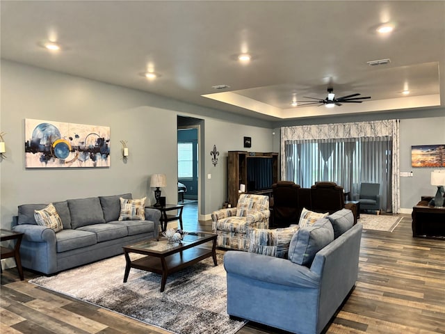 living room featuring dark hardwood / wood-style floors, ceiling fan, and a raised ceiling