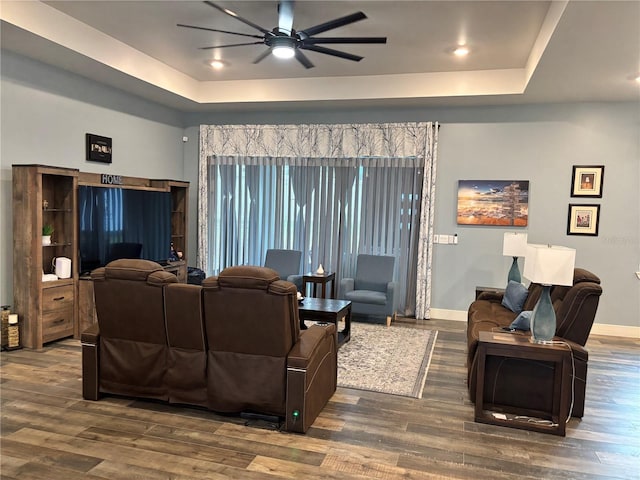 living room featuring dark wood-type flooring, a tray ceiling, and ceiling fan