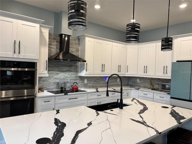 kitchen featuring pendant lighting, white cabinets, light stone counters, and wall chimney range hood