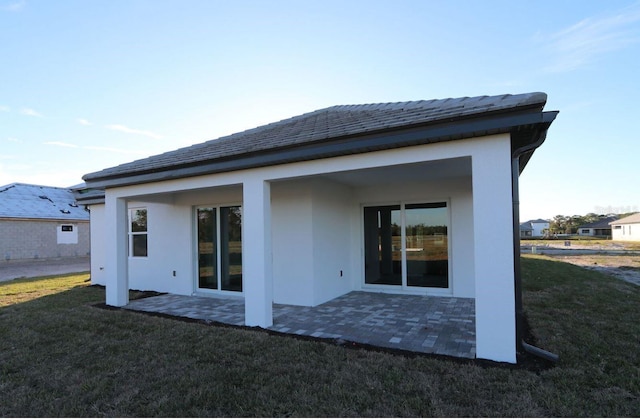 back of house featuring a patio area, a lawn, and stucco siding