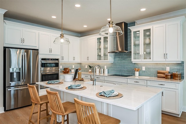 kitchen with wall chimney exhaust hood, a kitchen island with sink, stainless steel appliances, and decorative light fixtures