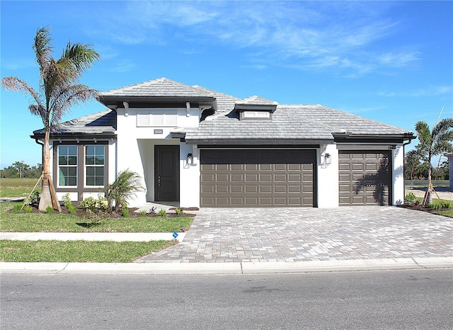 prairie-style home featuring a garage, decorative driveway, and stucco siding