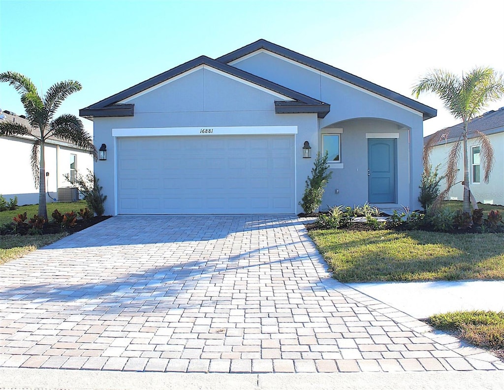 ranch-style home with a garage, decorative driveway, a front yard, and stucco siding