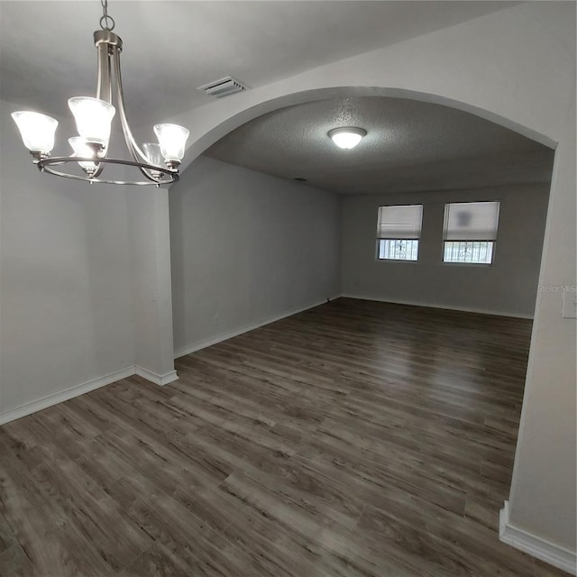 spare room with dark wood-type flooring, a chandelier, and a textured ceiling