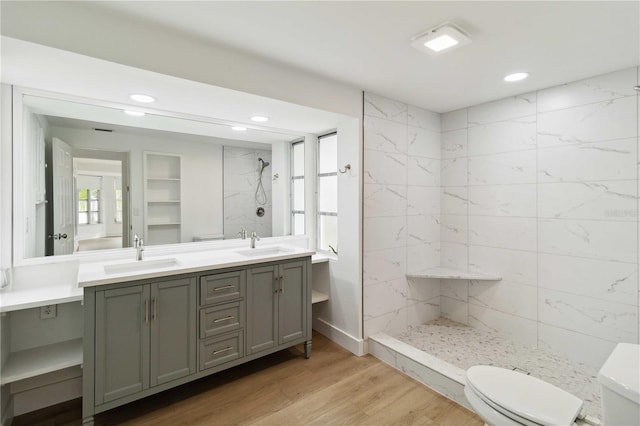 bathroom with wood-type flooring, toilet, vanity, and a tile shower