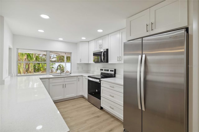 kitchen featuring appliances with stainless steel finishes, sink, white cabinets, light stone counters, and light hardwood / wood-style floors