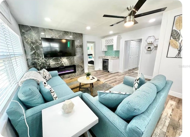 living room with a premium fireplace, beverage cooler, ceiling fan, and light hardwood / wood-style flooring