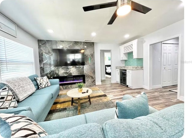 living room featuring a fireplace, beverage cooler, ceiling fan, and light wood-type flooring