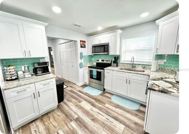 kitchen featuring stainless steel appliances, light hardwood / wood-style floors, backsplash, white cabinetry, and sink