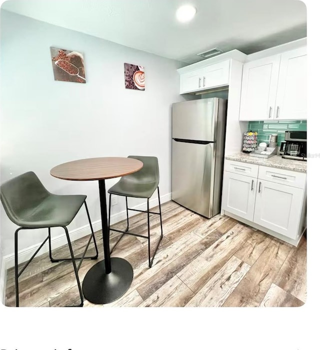 kitchen featuring stainless steel refrigerator, backsplash, and white cabinetry