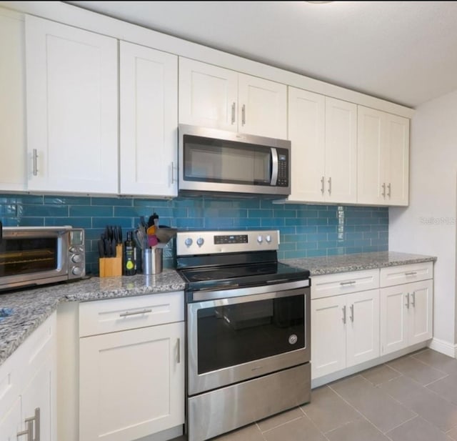 kitchen with decorative backsplash, light tile patterned floors, white cabinetry, and appliances with stainless steel finishes