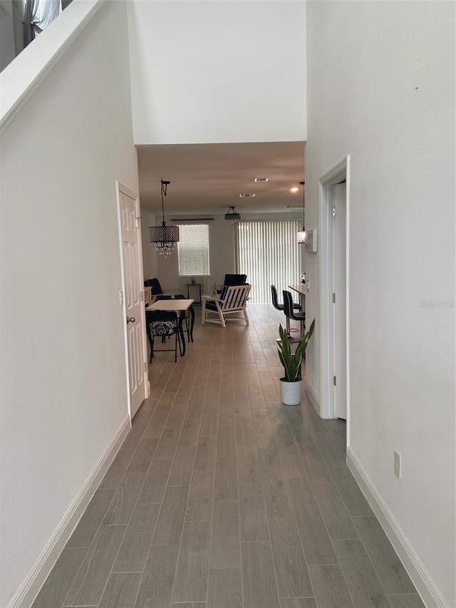 hallway with a notable chandelier, wood-type flooring, and a high ceiling