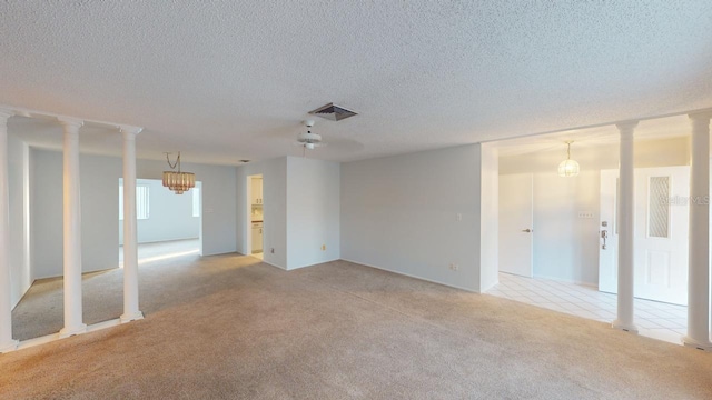 spare room with light colored carpet, a textured ceiling, and ornate columns