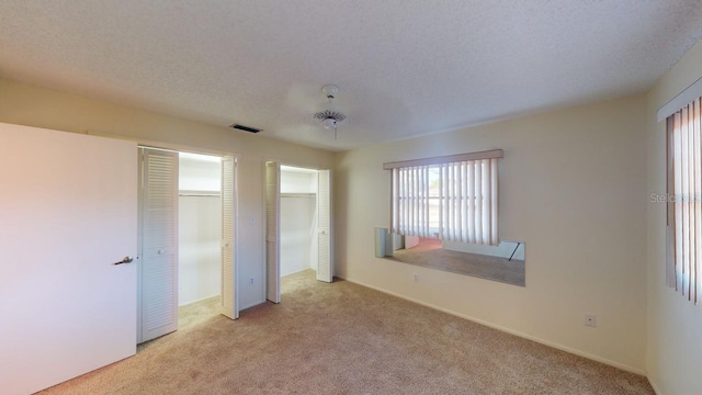 unfurnished bedroom featuring two closets, light carpet, and a textured ceiling