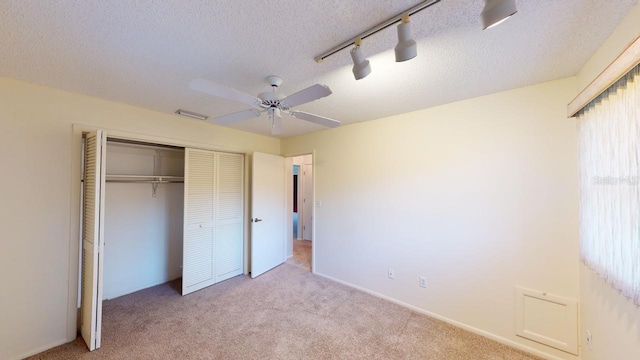 unfurnished bedroom with ceiling fan, track lighting, a textured ceiling, light colored carpet, and a closet