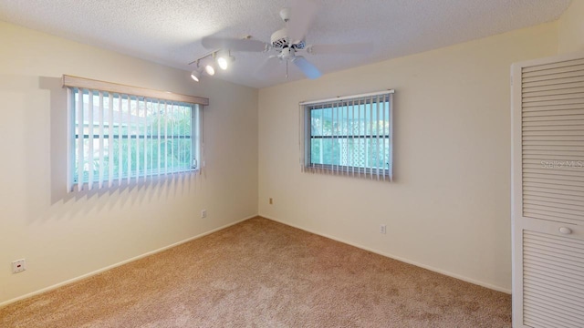 carpeted empty room featuring ceiling fan, track lighting, and a textured ceiling