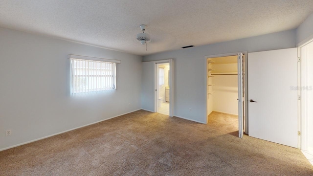 unfurnished bedroom featuring ceiling fan, a spacious closet, light colored carpet, and a textured ceiling