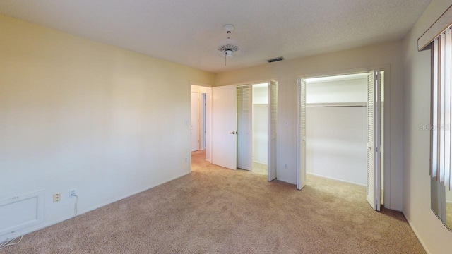 unfurnished bedroom featuring two closets, light colored carpet, and a textured ceiling