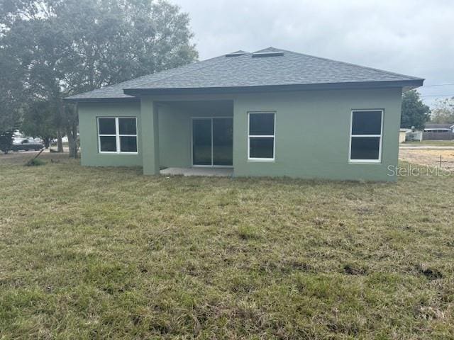 back of house with a shingled roof, a lawn, and stucco siding