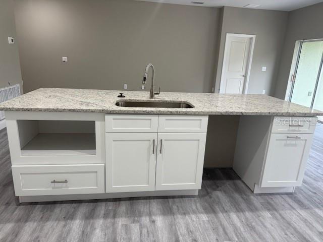 kitchen with light stone countertops, a sink, light wood-style flooring, and white cabinets