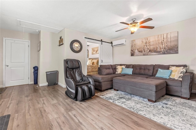 living room featuring light hardwood / wood-style flooring, a wall unit AC, a barn door, and ceiling fan