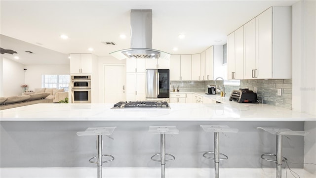 kitchen with a breakfast bar, kitchen peninsula, island exhaust hood, stainless steel appliances, and white cabinets