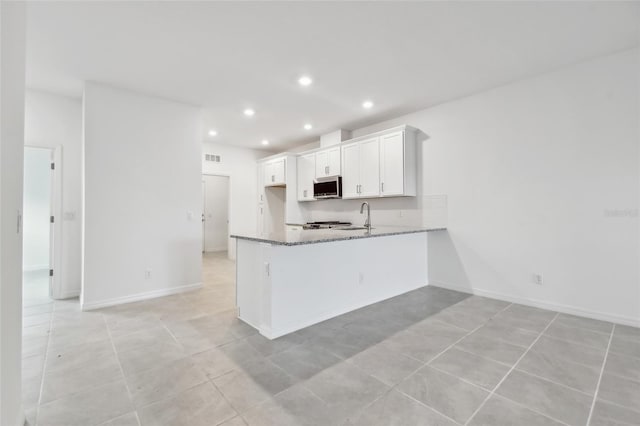 kitchen with stone countertops, light tile patterned floors, white cabinets, and kitchen peninsula