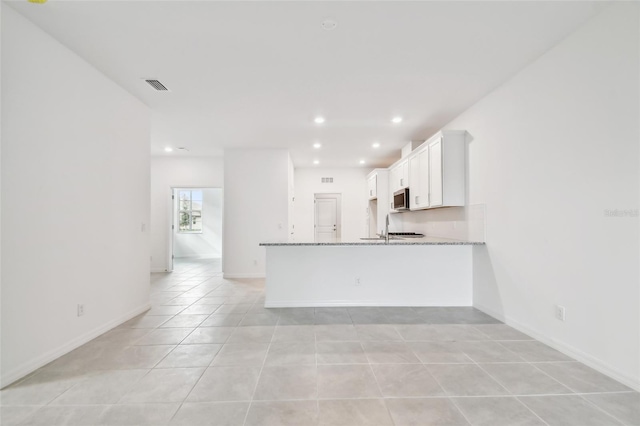 kitchen with sink, white cabinets, light tile patterned floors, kitchen peninsula, and light stone countertops