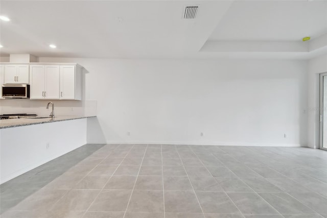 kitchen featuring white cabinetry, a raised ceiling, light stone counters, and light tile patterned floors