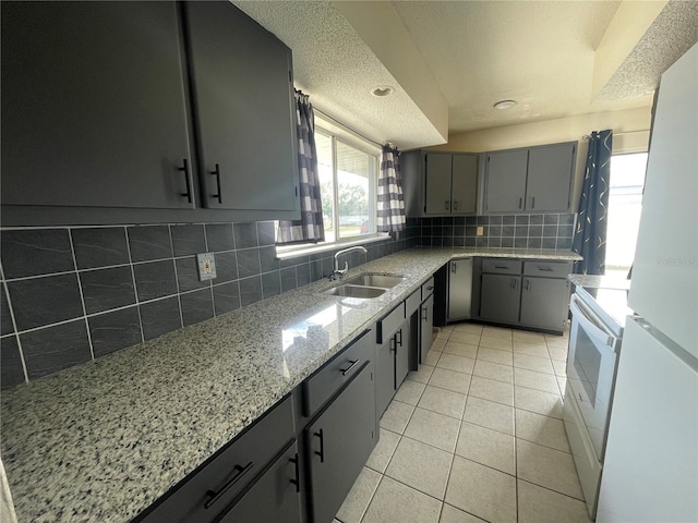 kitchen featuring sink, light tile patterned floors, gray cabinets, white appliances, and backsplash