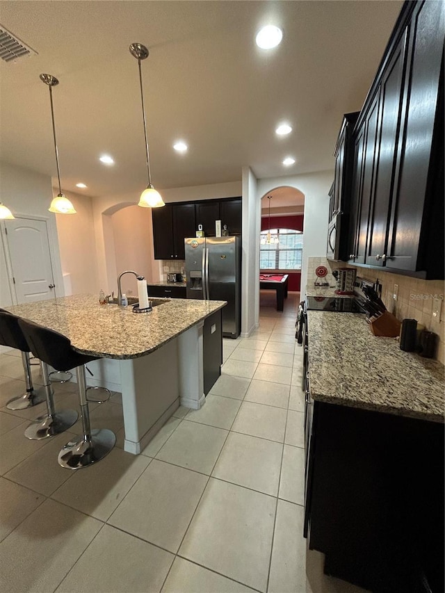 kitchen featuring sink, light tile patterned floors, appliances with stainless steel finishes, an island with sink, and pendant lighting