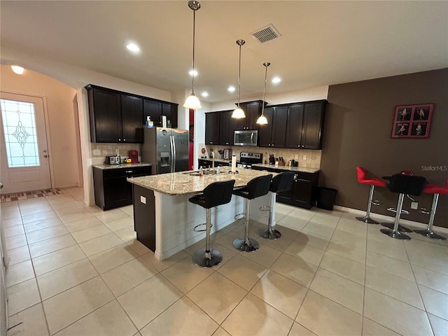 kitchen with appliances with stainless steel finishes, a kitchen island with sink, and light tile patterned floors