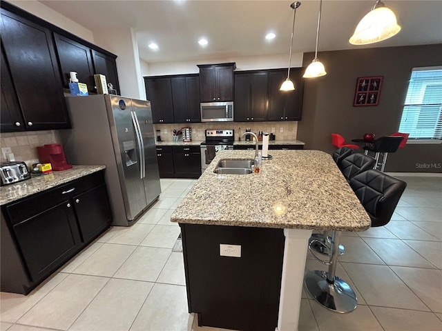 kitchen with sink, a breakfast bar area, hanging light fixtures, stainless steel appliances, and a center island with sink