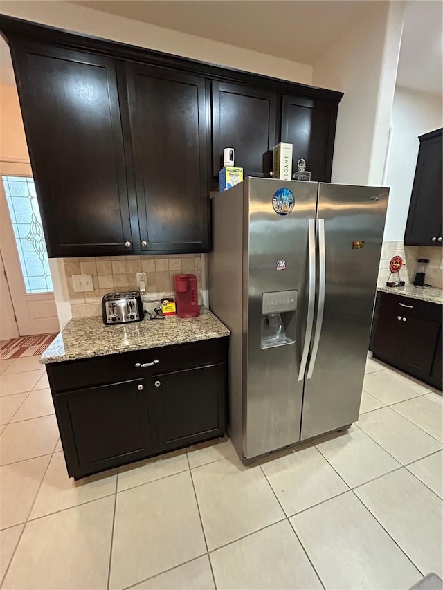 kitchen with light tile patterned flooring, light stone countertops, stainless steel fridge, and backsplash