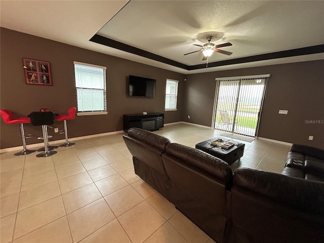 tiled living room with a textured ceiling, a raised ceiling, and ceiling fan