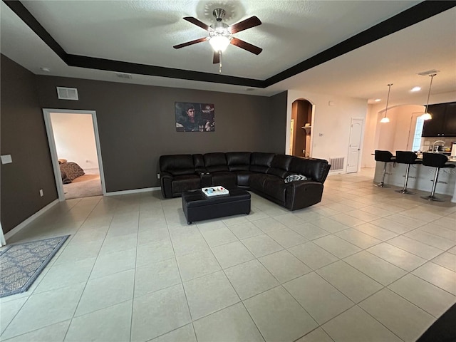 tiled living room with a raised ceiling and ceiling fan