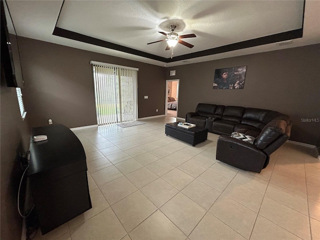 living room with light tile patterned flooring, ceiling fan, a raised ceiling, and a textured ceiling