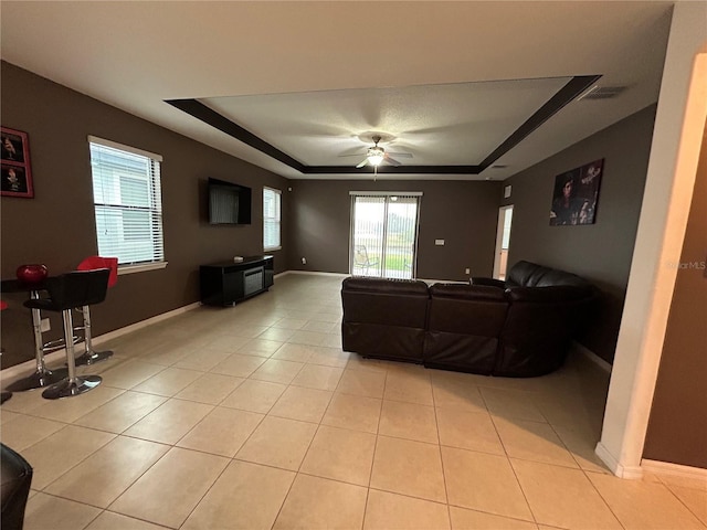 living room with ceiling fan, a tray ceiling, and light tile patterned floors