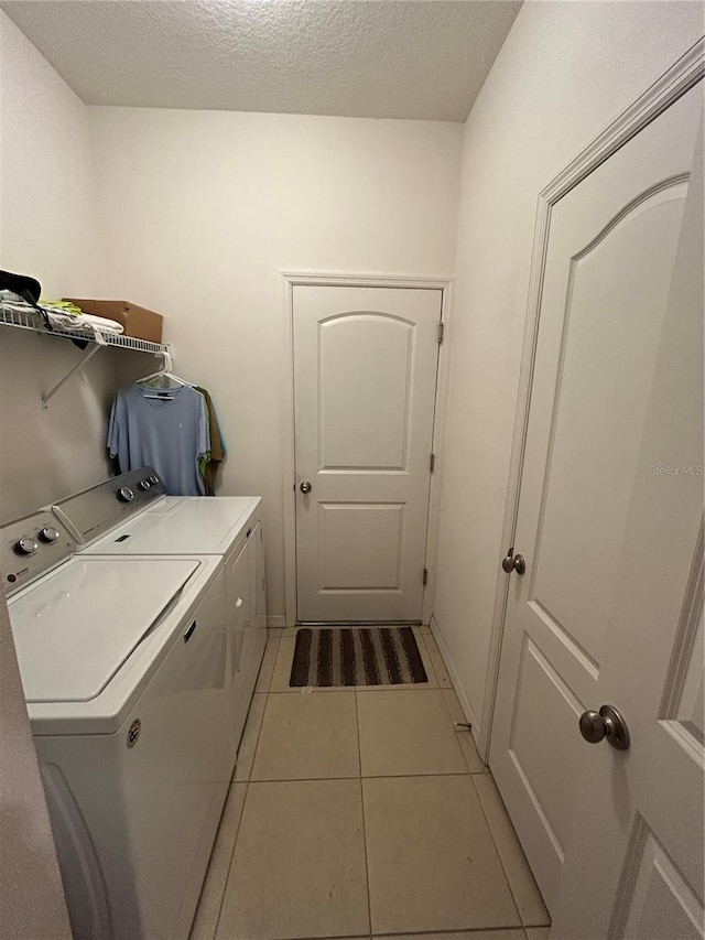 clothes washing area featuring light tile patterned flooring, independent washer and dryer, and a textured ceiling