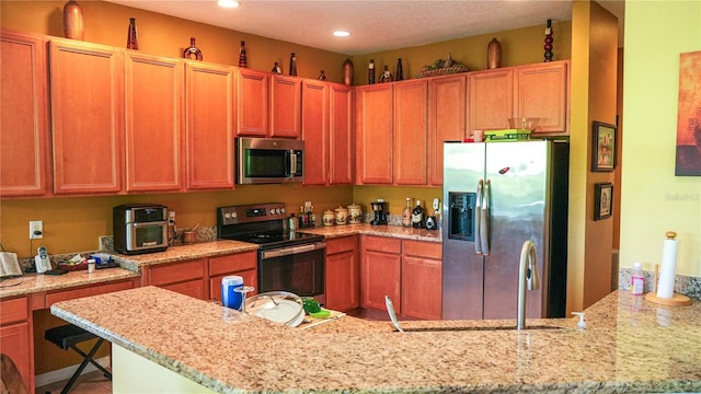 kitchen with a kitchen bar, light stone countertops, kitchen peninsula, and appliances with stainless steel finishes