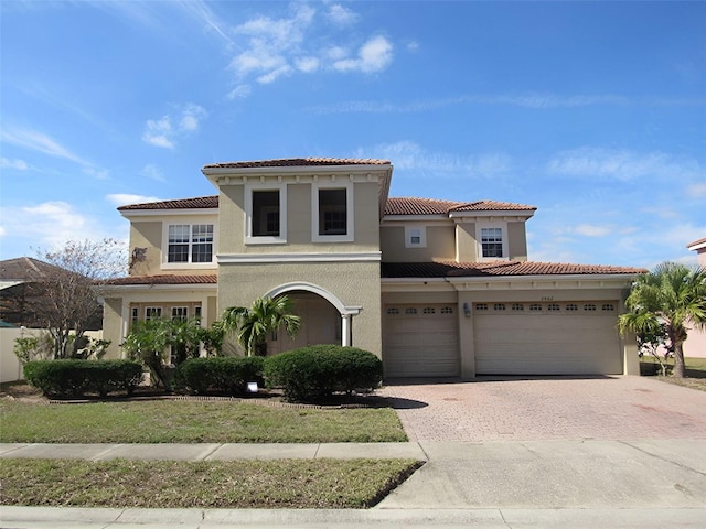 mediterranean / spanish home featuring a tiled roof, decorative driveway, and stucco siding