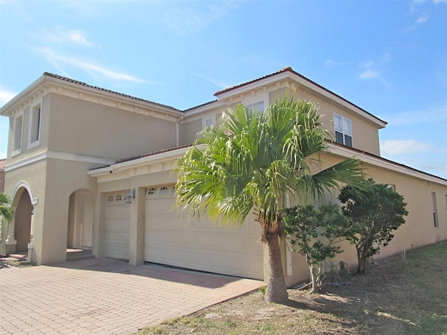 mediterranean / spanish-style house featuring stucco siding, decorative driveway, and a garage