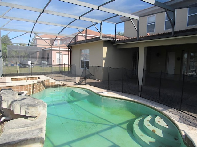 outdoor pool featuring glass enclosure, an in ground hot tub, and a patio