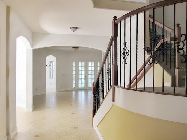 stairway featuring arched walkways, french doors, and baseboards