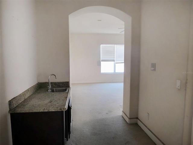 hall with arched walkways, light colored carpet, baseboards, and a sink