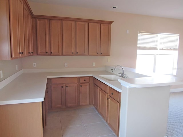 kitchen featuring a peninsula, light tile patterned floors, light countertops, and a sink