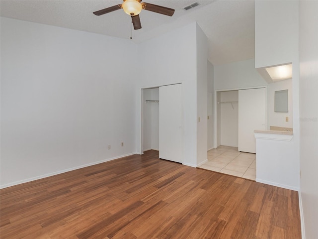 unfurnished living room featuring ceiling fan, light hardwood / wood-style floors, and a high ceiling