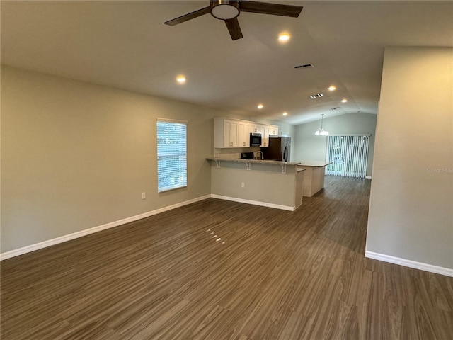 kitchen featuring black fridge, dark hardwood / wood-style floors, white cabinets, a kitchen bar, and kitchen peninsula