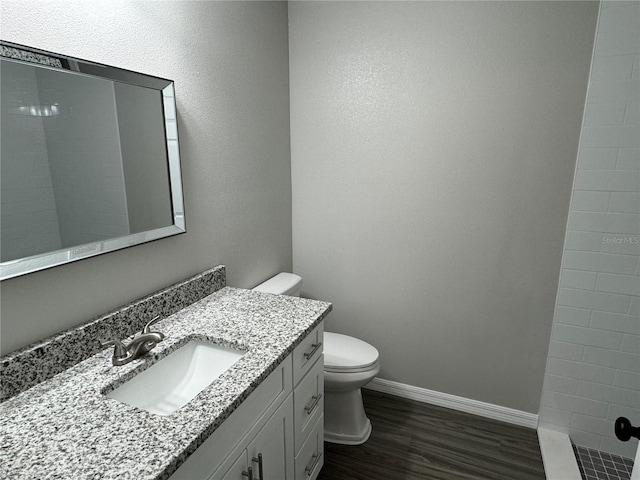 bathroom with vanity, wood-type flooring, tiled shower, and toilet